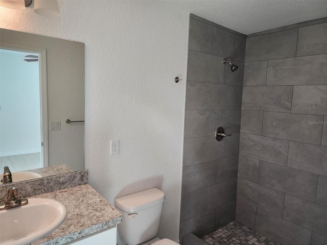 full bathroom featuring a textured ceiling, a textured wall, toilet, vanity, and tiled shower