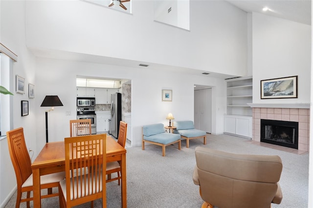 dining area with visible vents, a tiled fireplace, a towering ceiling, and light colored carpet