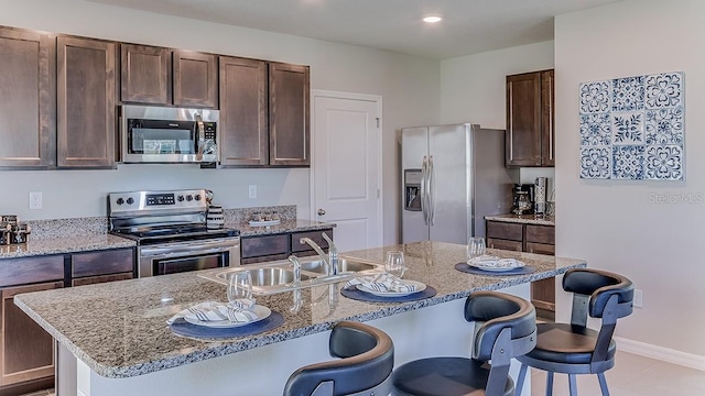 kitchen featuring a breakfast bar area, stainless steel appliances, a sink, an island with sink, and light stone countertops