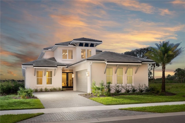 prairie-style home featuring decorative driveway, a tile roof, stucco siding, an attached garage, and a front yard