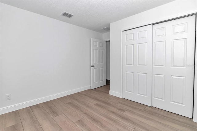 unfurnished bedroom featuring visible vents, baseboards, light wood-style flooring, a textured ceiling, and a closet