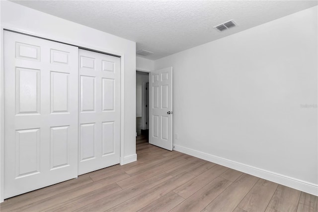 unfurnished bedroom with light wood finished floors, baseboards, visible vents, and a closet