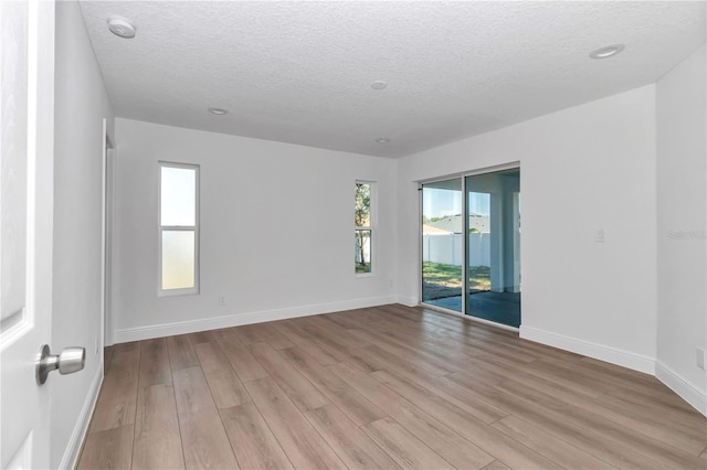 empty room with light wood-type flooring, a textured ceiling, and baseboards