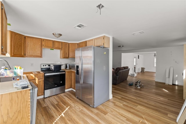 kitchen featuring stainless steel appliances, light countertops, light wood-style flooring, open floor plan, and a sink