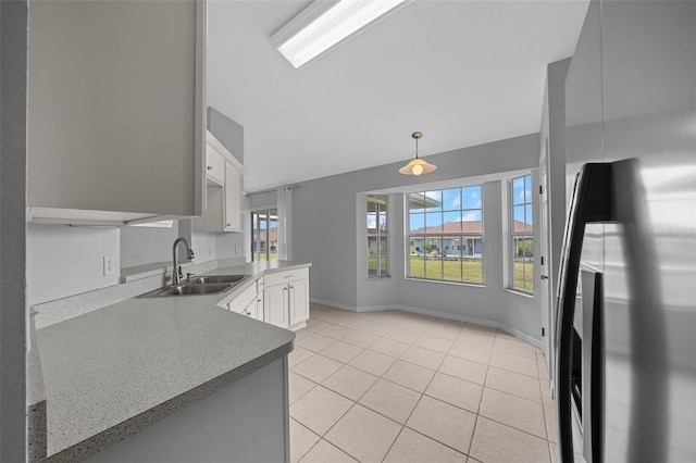 kitchen with light tile patterned floors, baseboards, white cabinets, stainless steel refrigerator, and a sink