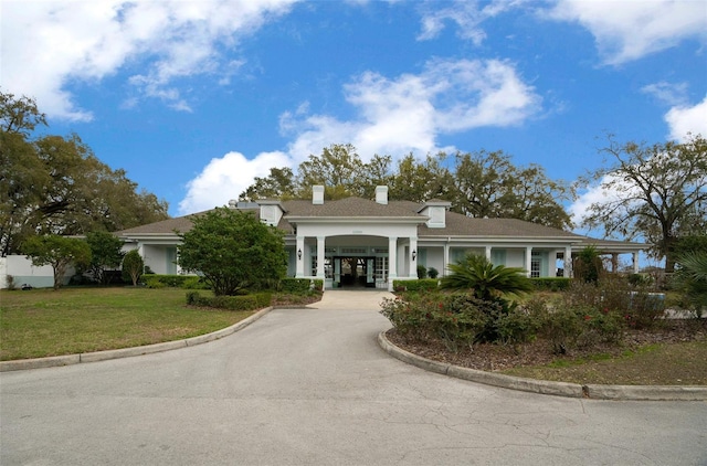 view of front of property featuring driveway, a chimney, a front lawn, and stucco siding