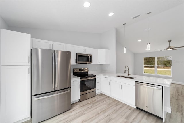 kitchen with lofted ceiling, a peninsula, a sink, white cabinets, and appliances with stainless steel finishes