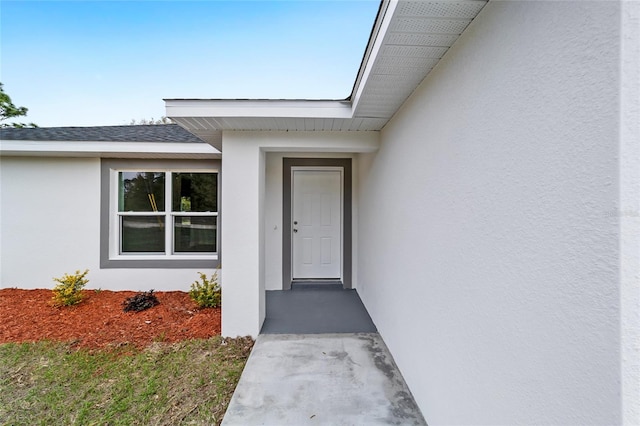 doorway to property with roof with shingles and stucco siding