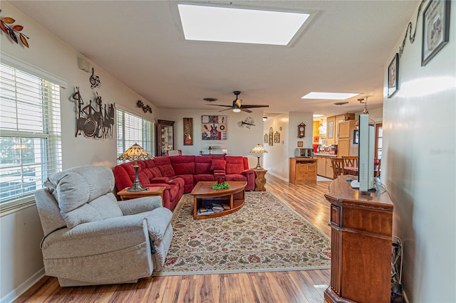 living room featuring a skylight, baseboards, a ceiling fan, and wood finished floors