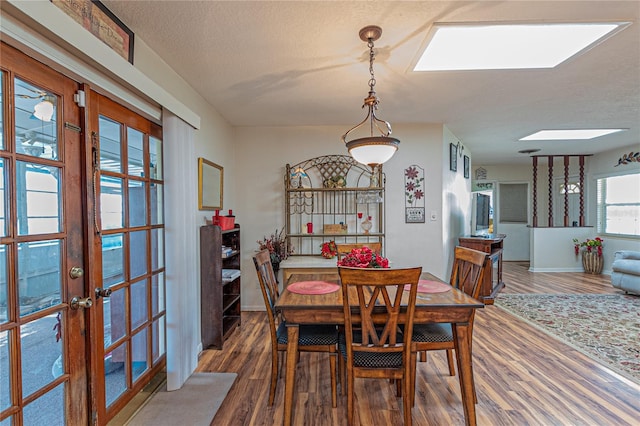 dining space featuring dark wood-style floors, a textured ceiling, a skylight, and baseboards