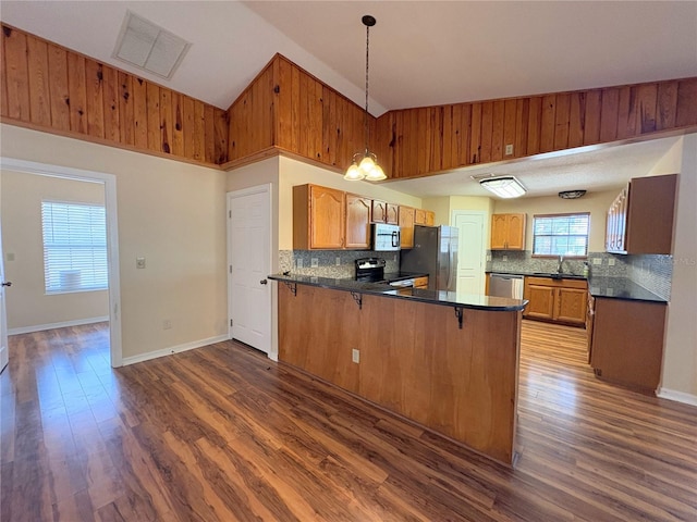 kitchen with visible vents, dark countertops, a peninsula, stainless steel appliances, and a sink