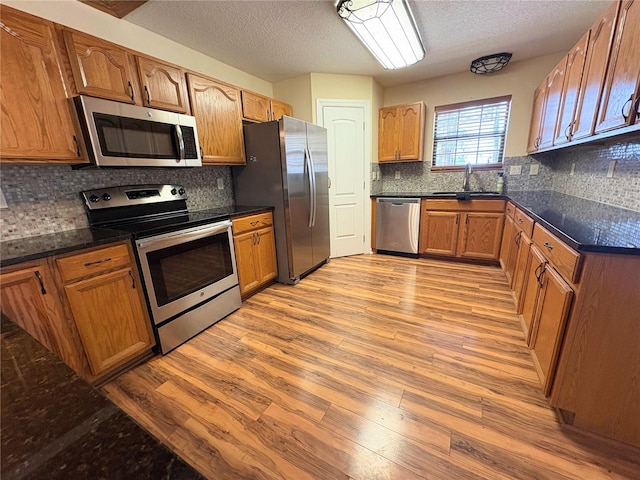 kitchen featuring light wood finished floors, decorative backsplash, appliances with stainless steel finishes, brown cabinets, and a sink