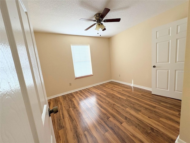 spare room with a textured ceiling, dark wood-style flooring, a ceiling fan, and baseboards