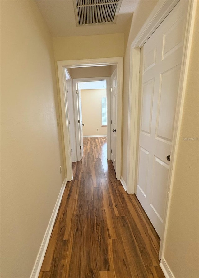 hallway featuring dark wood-style flooring, visible vents, and baseboards