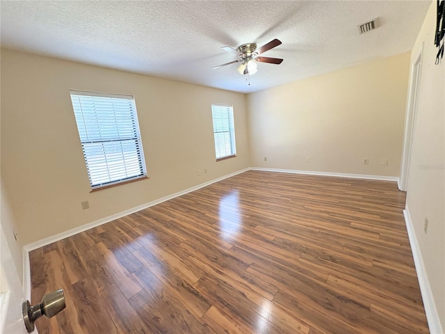 empty room with baseboards, visible vents, dark wood finished floors, and a textured ceiling