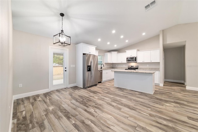 kitchen with appliances with stainless steel finishes, a kitchen island, white cabinets, and pendant lighting