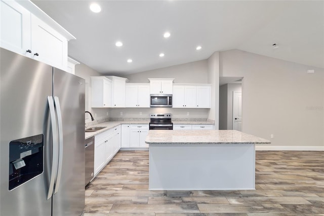 kitchen featuring light stone counters, a center island, appliances with stainless steel finishes, white cabinetry, and a sink