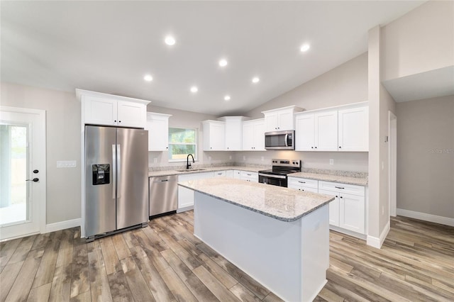 kitchen with appliances with stainless steel finishes, white cabinets, light stone counters, and a center island