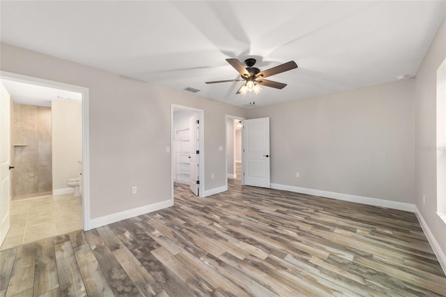 unfurnished bedroom featuring baseboards, visible vents, ensuite bath, and wood finished floors