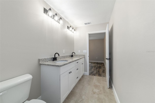 bathroom featuring toilet, double vanity, a sink, and visible vents