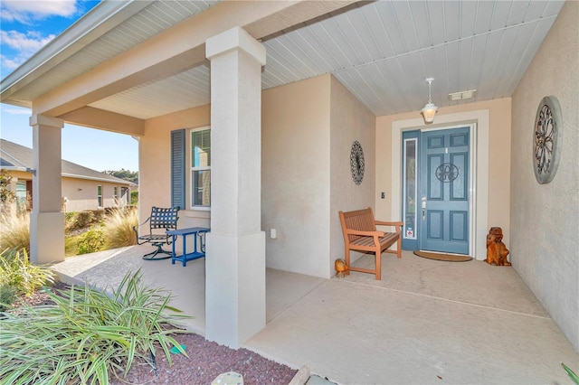 view of exterior entry with a porch, visible vents, and stucco siding