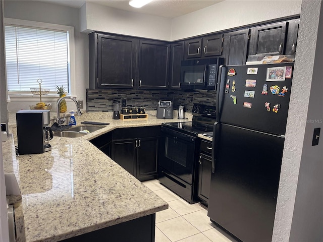 kitchen featuring light tile patterned floors, a sink, light stone countertops, dark cabinetry, and black appliances