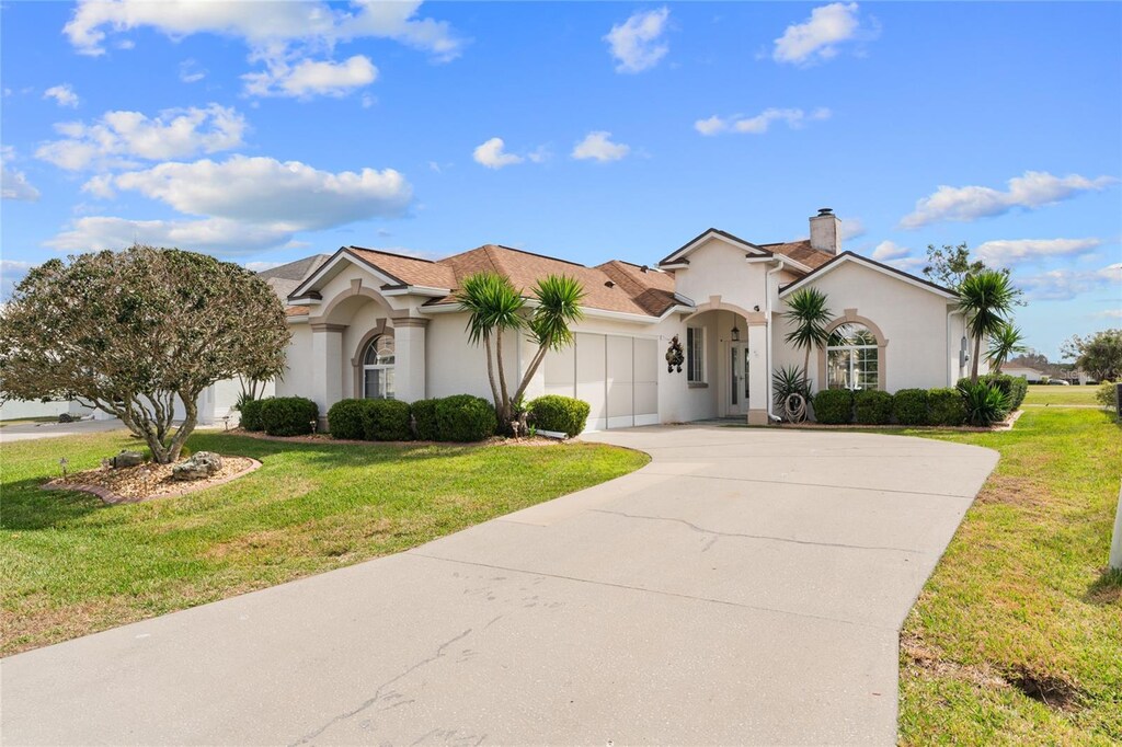 mediterranean / spanish-style home featuring a chimney, stucco siding, an attached garage, a front yard, and driveway