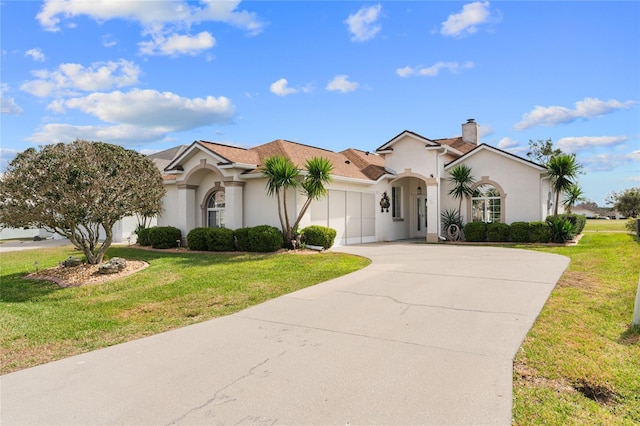 mediterranean / spanish-style home featuring a chimney, stucco siding, an attached garage, a front yard, and driveway