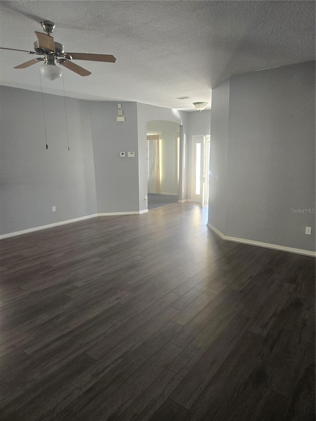 empty room with a textured ceiling, dark wood finished floors, a ceiling fan, and baseboards