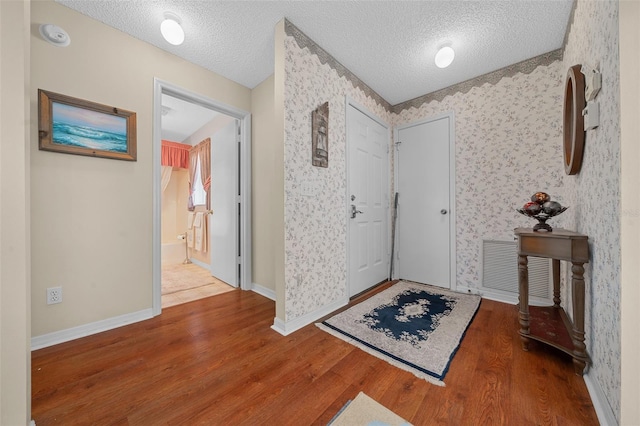 foyer entrance featuring wood finished floors, a textured ceiling, baseboards, and wallpapered walls