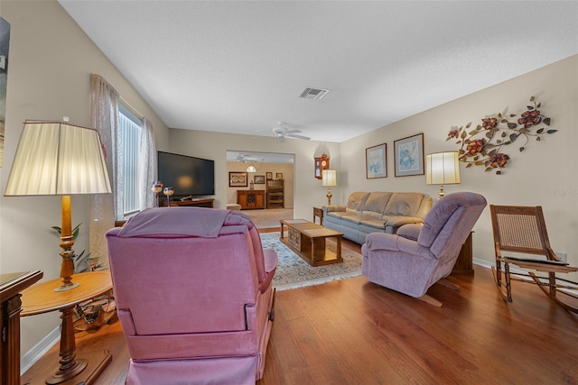 living area featuring baseboards, visible vents, a ceiling fan, wood finished floors, and a textured ceiling
