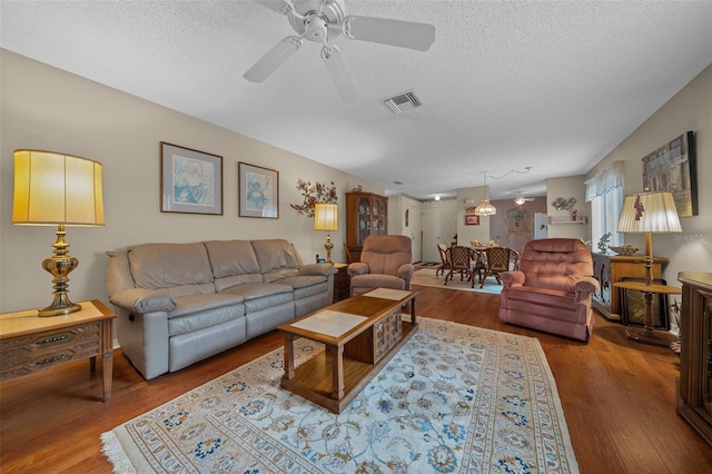 living room with a textured ceiling, ceiling fan, wood finished floors, and visible vents