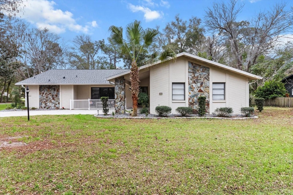 mid-century modern home with a front yard, stone siding, and covered porch