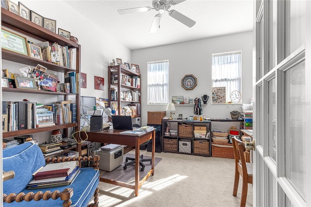 home office featuring a textured ceiling, a ceiling fan, and light colored carpet