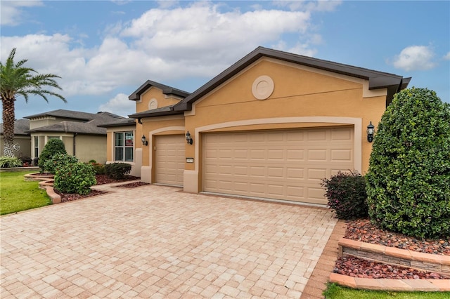 ranch-style house featuring decorative driveway, an attached garage, and stucco siding