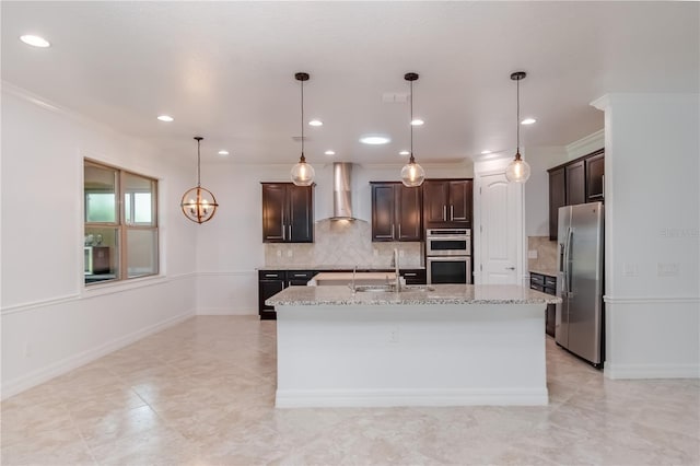 kitchen with dark brown cabinetry, wall chimney exhaust hood, appliances with stainless steel finishes, light stone countertops, and a sink