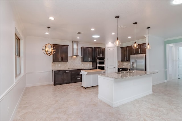 kitchen with dark brown cabinetry, a kitchen island with sink, stainless steel appliances, wall chimney range hood, and a sink