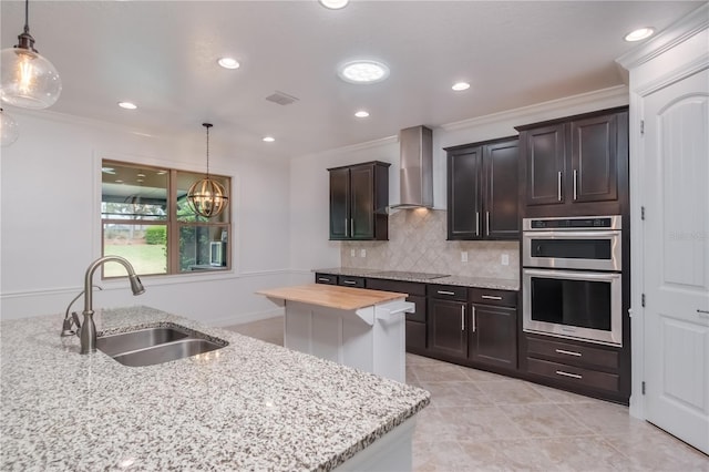 kitchen with crown molding, tasteful backsplash, double oven, a sink, and wall chimney exhaust hood