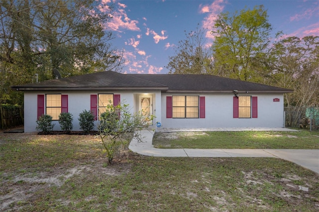 ranch-style house with fence, a lawn, and stucco siding