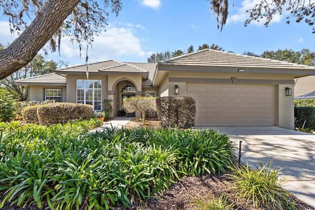 view of front of house featuring a garage, concrete driveway, a tiled roof, and stucco siding