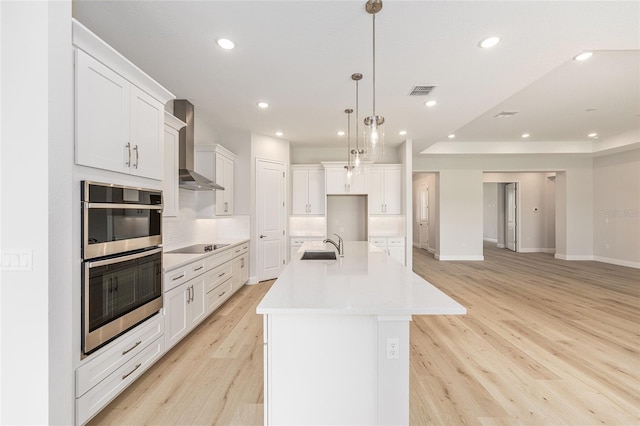 1929 NW 85th Loop, Ocala, FL 34475 - kitchen featuring wall chimney exhaust hood, double oven, light wood finished floors, a large island with sink, and white cabinetry