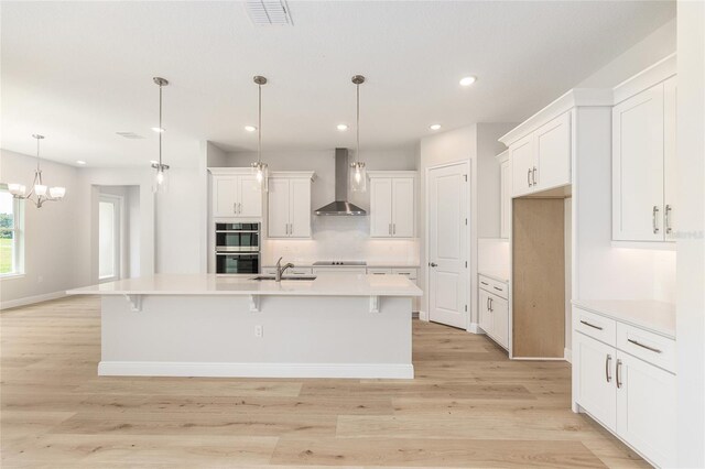 1929 NW 85th Loop, Ocala, FL 34475 - kitchen featuring wall chimney exhaust hood, white cabinetry, light wood finished floors, backsplash, and a large island with sink