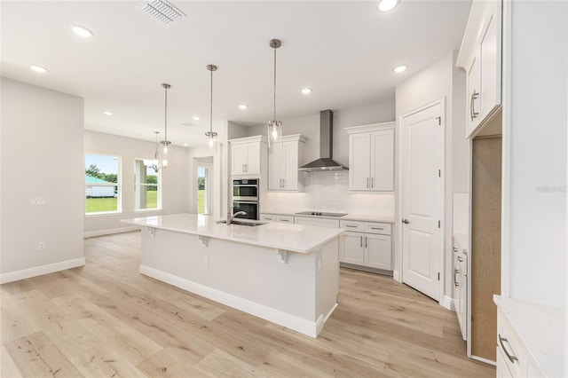 1929 NW 85th Loop, Ocala, FL 34475 - kitchen featuring wall chimney range hood, black electric cooktop, stainless steel double oven, light wood-style flooring, and tasteful backsplash