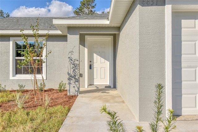 property entrance with roof with shingles and stucco siding