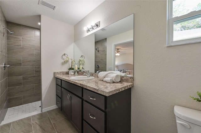 bathroom with visible vents, a textured wall, toilet, vanity, and walk in shower