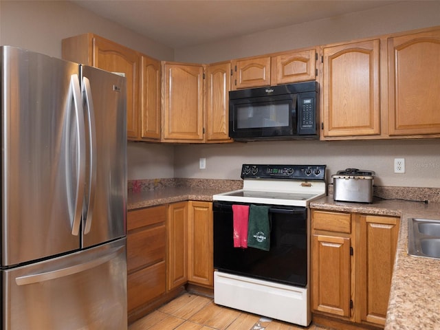 kitchen featuring light countertops, freestanding refrigerator, a sink, range with electric cooktop, and black microwave