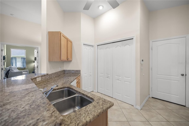 kitchen with light tile patterned floors, ceiling fan, a high ceiling, a sink, and dark countertops