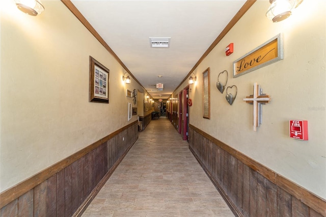 corridor with wooden walls, visible vents, and wainscoting