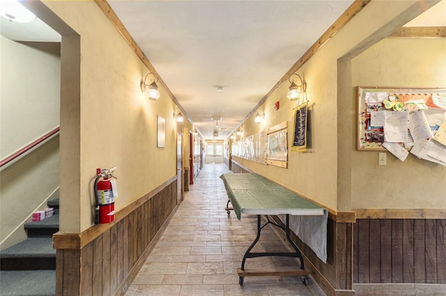 hall with stairs, a textured wall, wainscoting, and wooden walls