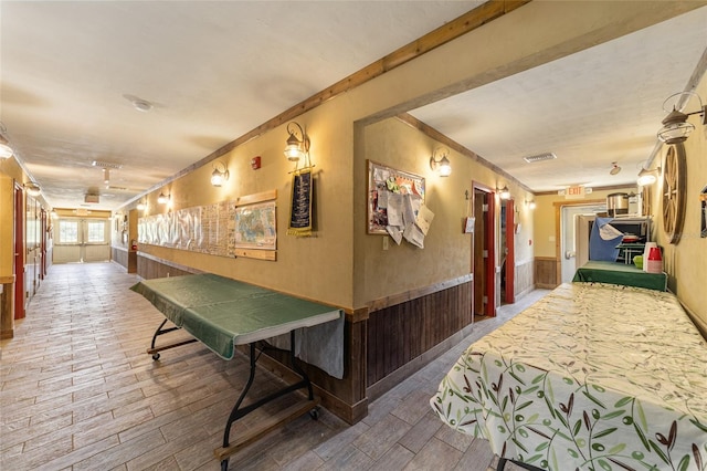 corridor featuring ornamental molding, wainscoting, visible vents, and wood finished floors